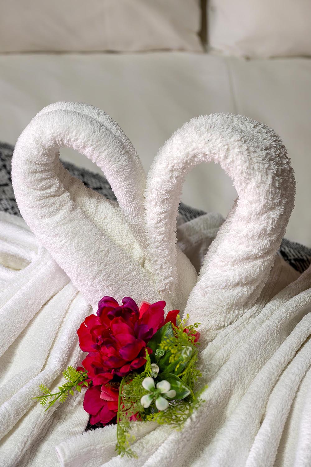 Handtuchschwäne und Blumen auf dem Bett arrangiert
