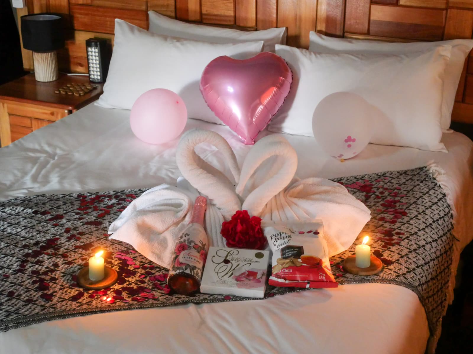 Romantic package arranged on a bed with wine, treats, balloons and candles